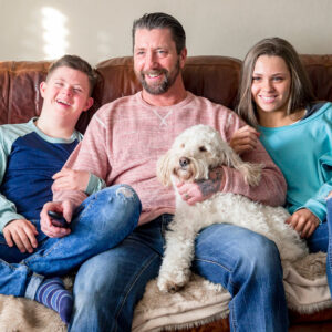 Dad and two children sitting on sofa with a dog on their lap